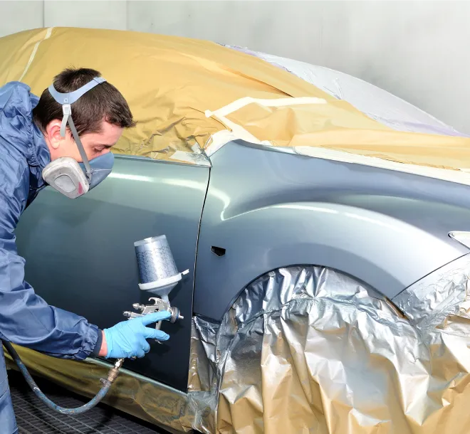 Close-up of a spray gun refinishing a car door with the rest of the vehicle masked off